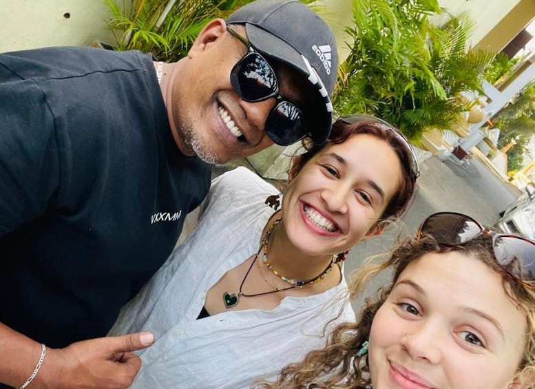Three people outdoors, one wearing a black shirt with white text, another in a white shirt, and the third in a black cap. 4