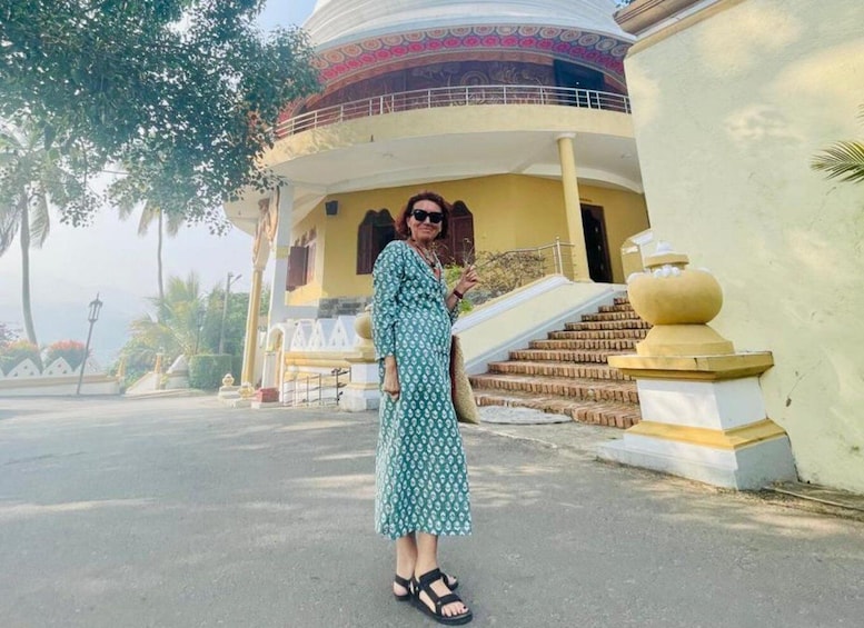 A woman in a patterned dress standing in front of a building with a staircase and a decorative balustrade. 5