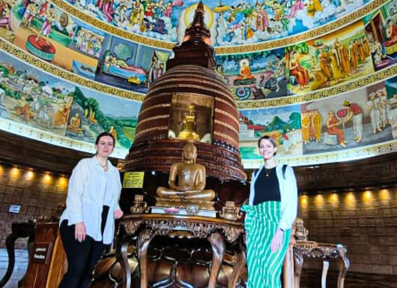 A large Buddha statue in a temple with a detailed mural on the ceiling. 2