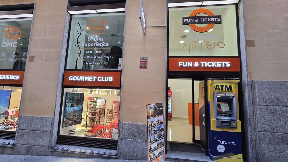 Een gebouw met een 'Gourmet Club' bord, een 'Fun & Tickets' bord, een pinautomaat en een 'DMC' bord. 2