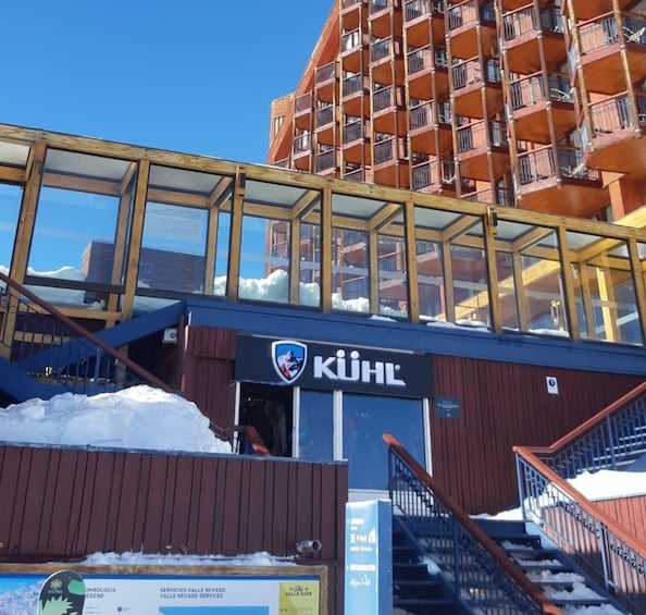 A ski resort entrance with a glass bridge, a ski lift, and a building with the logo 'KÜHL'. 4