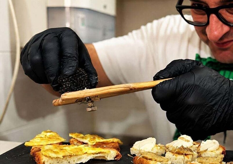 A person wearing black gloves using a wooden tool to cut food items on a black surface. 4