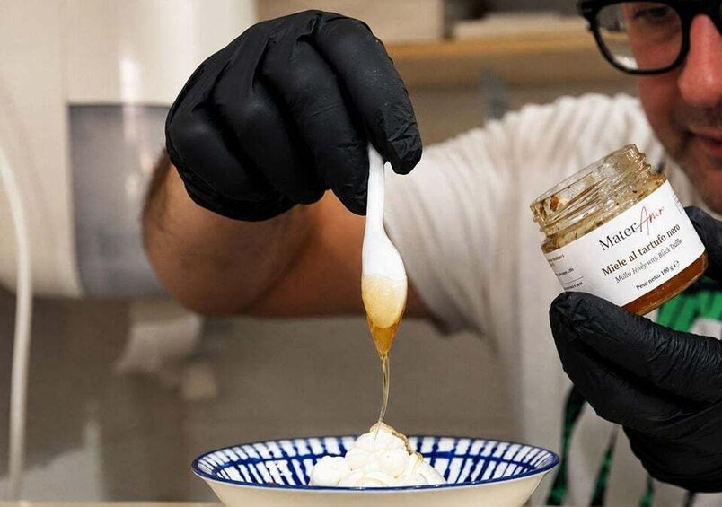 A person wearing black gloves holding a jar labeled 'Miele al tartufo nero' and pouring a white substance into a bowl. 2