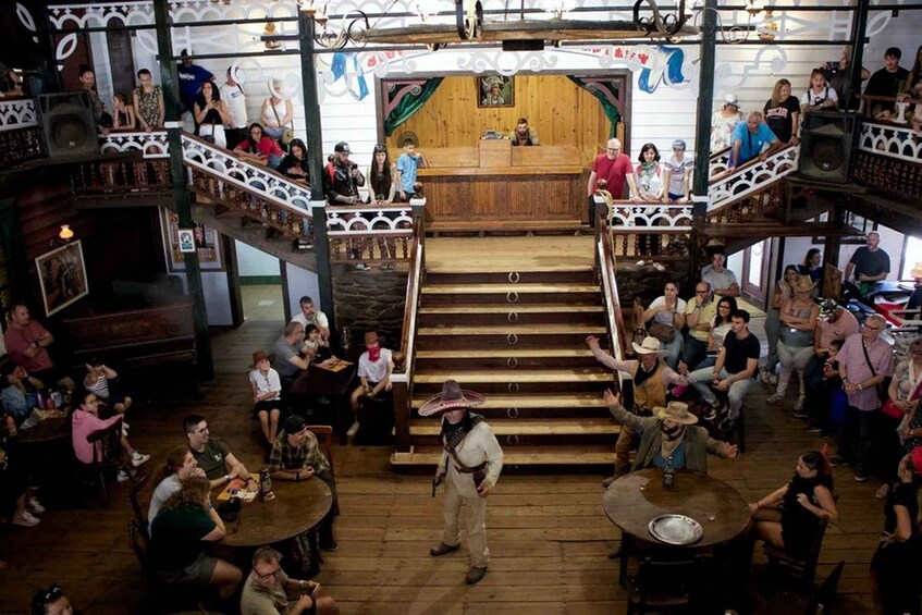 Un espacio interior concurrido con escaleras de madera, mesas y personas realizando diversas actividades. 3