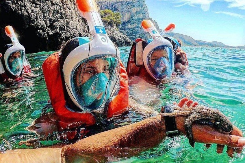 Two people snorkeling in clear water with rocky cliffs in the background. 3