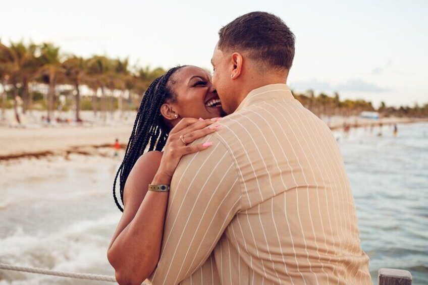 A couple embracing on a boat near a beach with palm trees and a clear sky. 1