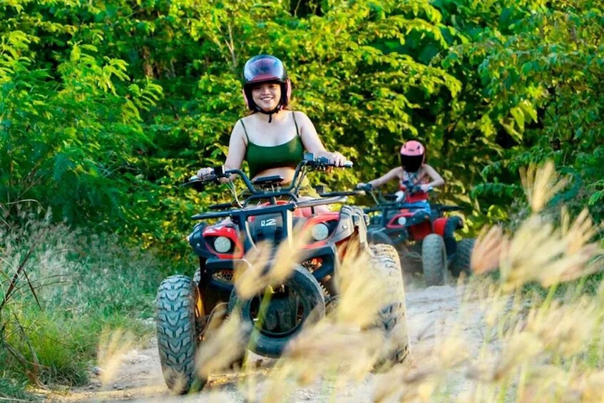 Zwei Personen fahren mit Quads auf einem Feldweg, der von Grünflächen gesäumt ist. 1