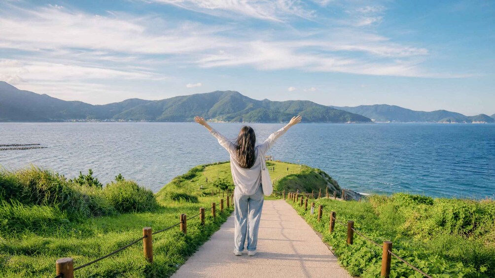 A person walking on a path with arms raised, overlooking a body of water and mountains. 4
