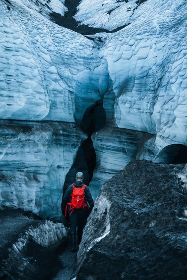 Une personne fait de la randonnée sur un glacier, portant un sac à dos rouge. 3