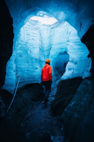 Une personne vêtue d’une veste rouge et d’un casque orange, à l’intérieur d’une grotte de glacier. 2