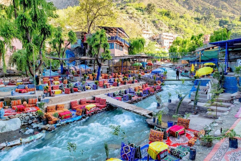 A riverside market with colorful textiles and a bridge over the flowing river. 5