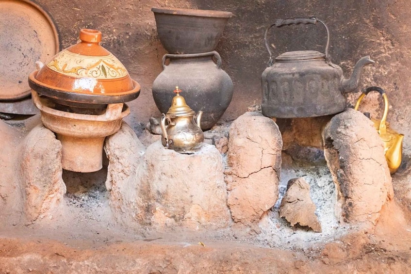 A collection of traditional cooking utensils, including a pot, a kettle, and a brass teapot, placed on a stone structure. 5