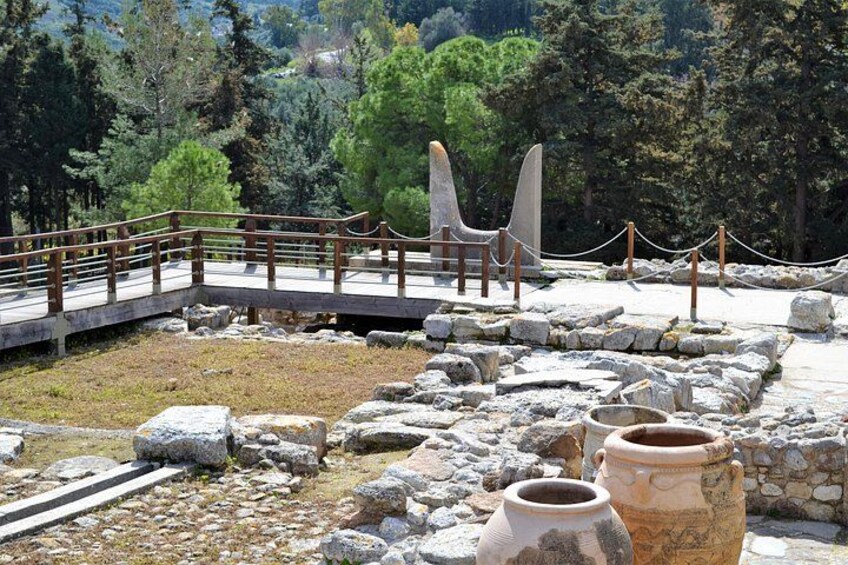 An archaeological site with stone ruins, pottery, and a wooden bridge. 2