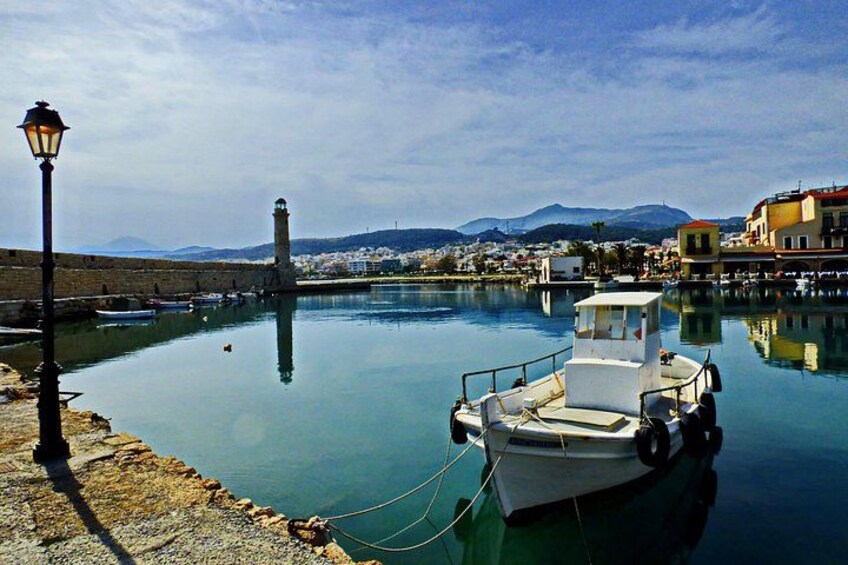 Un puerto tranquilo con un barco amarrado, un faro al fondo y una cadena montañosa al otro lado del agua. 4