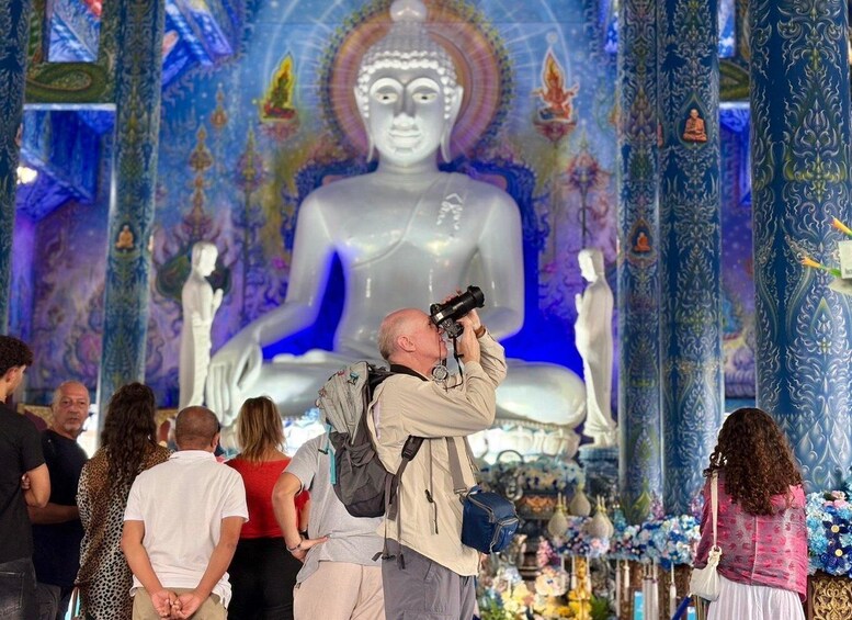 En man fotograferar en stor staty i ett tempel som är utsmyckat med detaljerade blå och guldiga dekorationer. 1