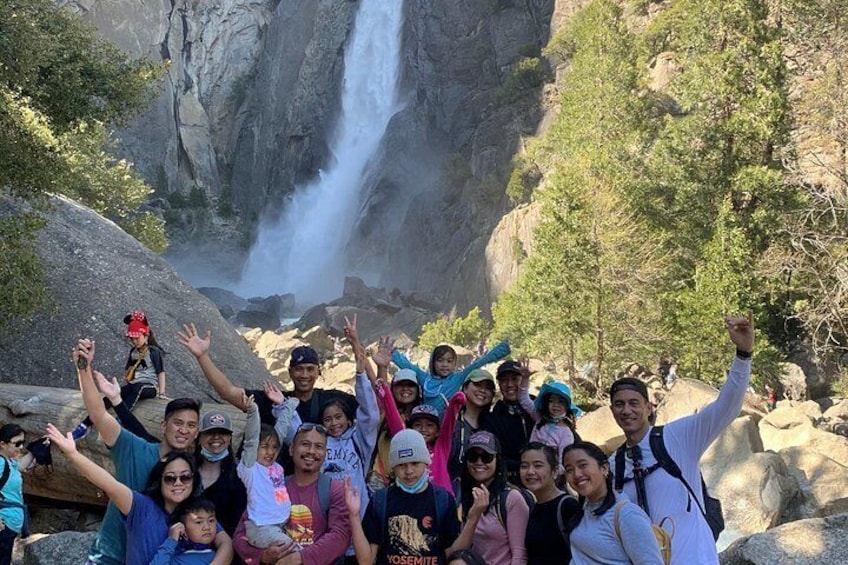 A group of people posing in front of a waterfall with a rocky landscape in the background. 2