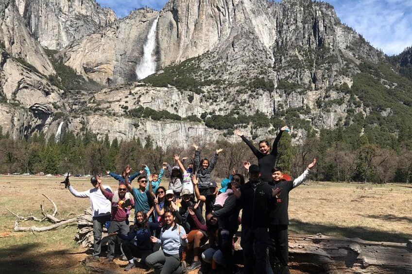 A group of people posing in front of a waterfall with mountains in the background. 2