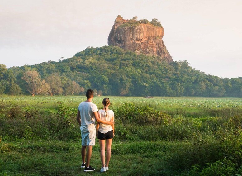 Two people standing in a field with a large rock formation in the background. 5