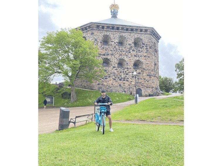 Una persona pedalea en bicicleta azul por un sendero cubierto de césped, con un edificio de piedra al fondo. 4