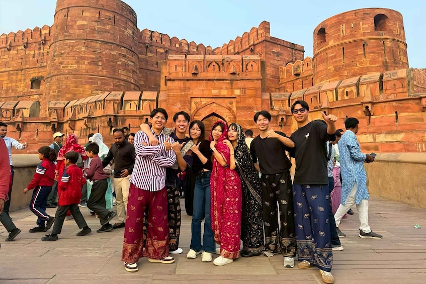 A group of people posing in front of a large, historic fort with red walls and intricate architecture. 5