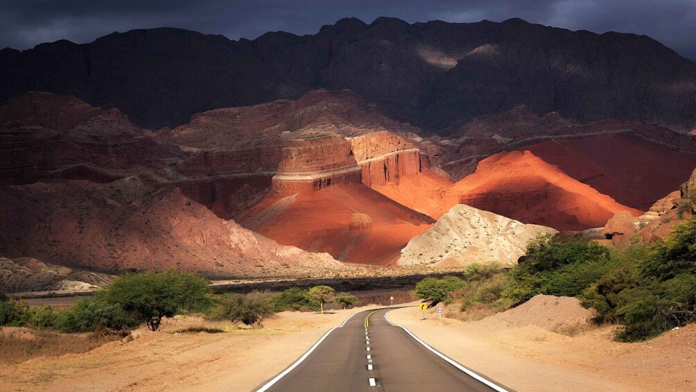 A road winding through a canyon with red rock formations and a mountain range in the background. 3