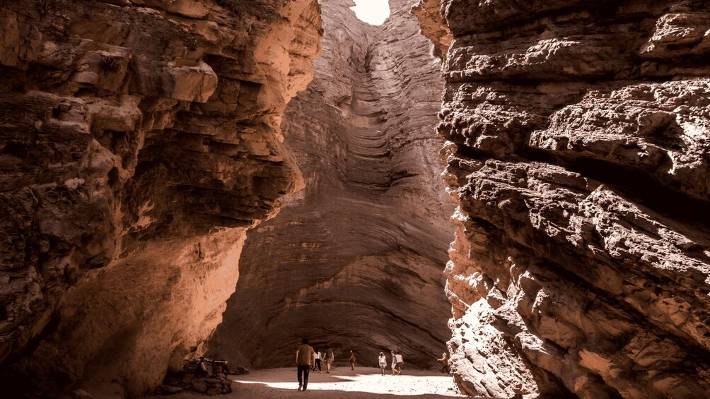 A canyon with layered rock formations and a group of people walking through. 2