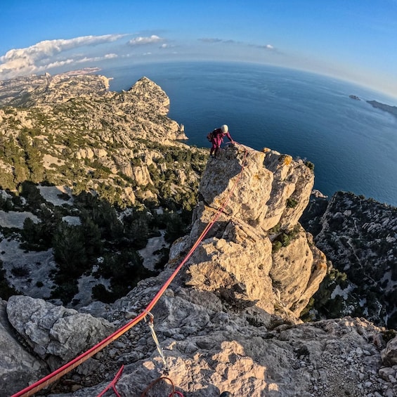 Una persona escala una montaña rocosa con una cuerda, con vistas a un paisaje costero. 5