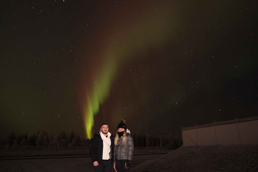Two people standing under a night sky with visible stars and a green aurora. 4