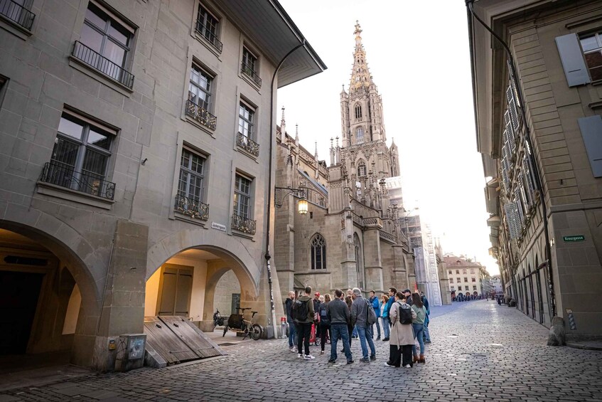 A cobblestone street with historic buildings, a church spire, and a group of people gathered in the center. 5