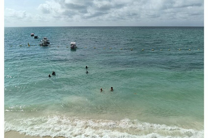 A beach with people swimming and boats in the water. 4