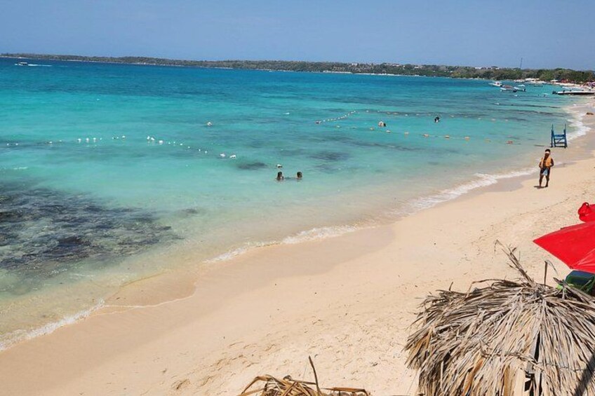 A beach with clear turquoise water, a sandy shore, and a few people swimming. 5