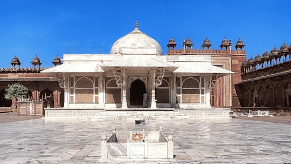 A white marble building with a large central dome and smaller domes, surrounded by a courtyard with a fountain. 2