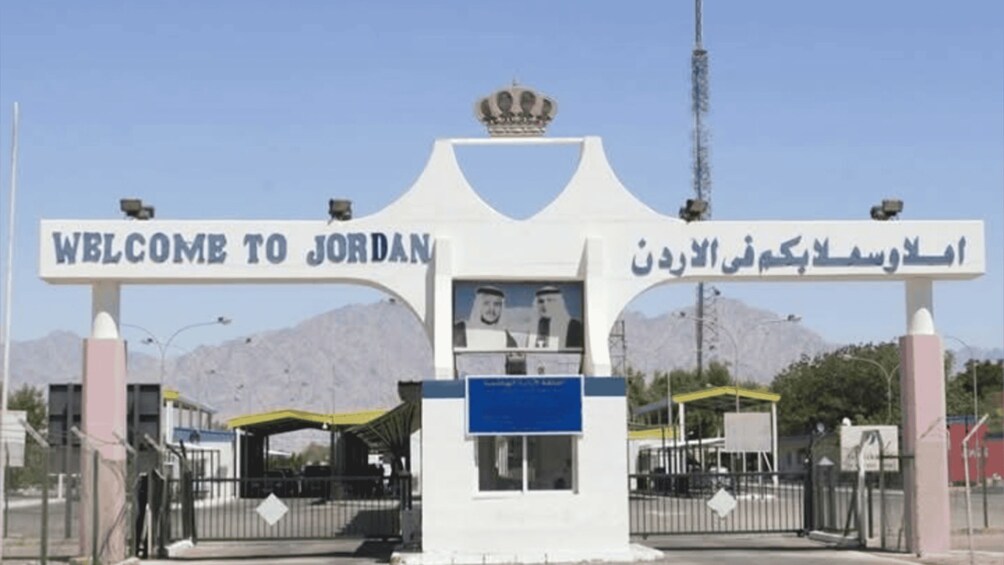 A welcome sign to Jordan with Arabic text, a gate, and mountains in the background. 2
