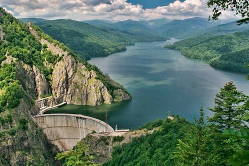 A dam with a spillway, surrounded by lush green hills and a calm lake. 2