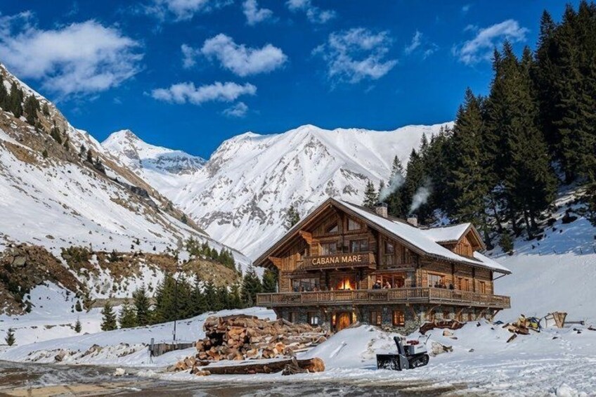 A wooden mountain lodge named 'Cabana Mare' surrounded by snow-covered mountains and pine trees. 1
