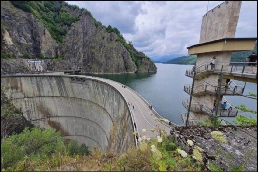 A large dam with a road curving around it, a bridge, and a body of water. 4