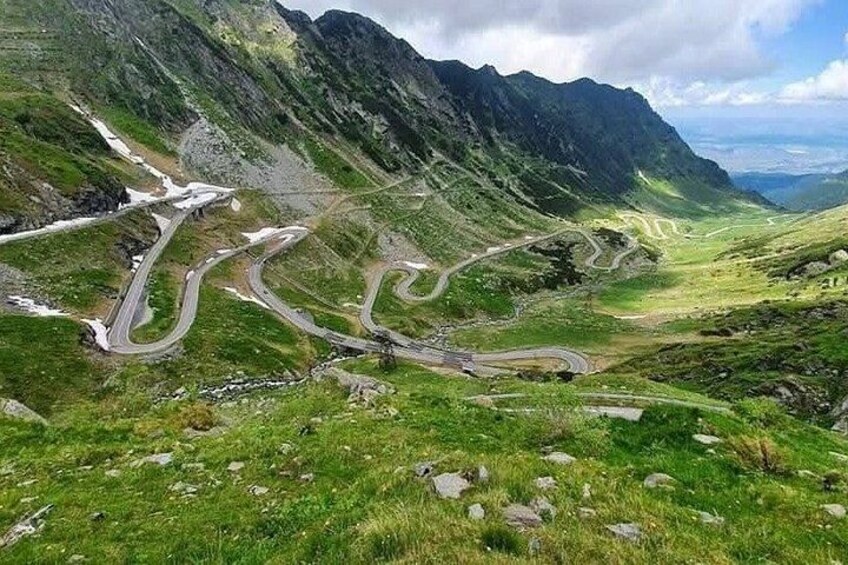 A winding mountain road surrounded by lush green hills and rocky mountains. 4
