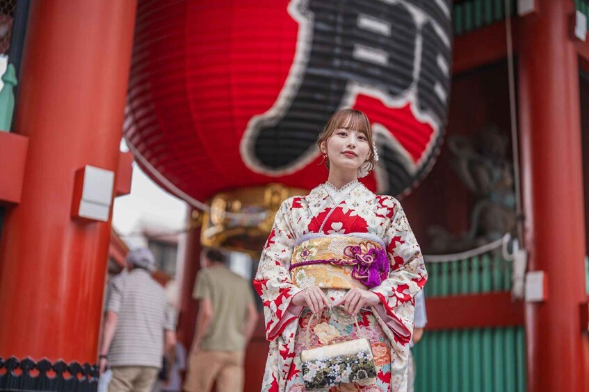 A person in traditional attire holding a patterned bag in front of a red lantern. 1