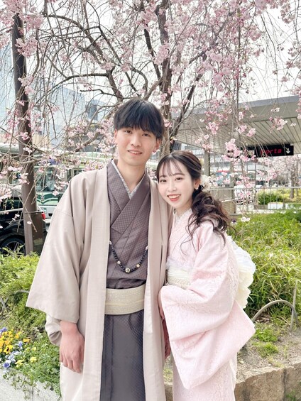 Two people in traditional attire standing in front of cherry blossoms. 4