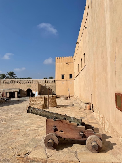 A historical site with a large cannon, stone walls, and palm trees. 2