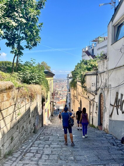 A narrow cobblestone street flanked by buildings with graffiti, leading towards a distant cityscape. 4