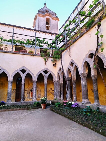 A courtyard with arched walkways, a bell tower, and climbing plants. 5