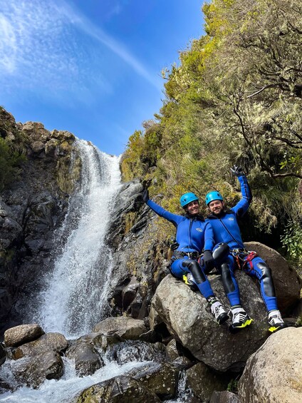 Two people in blue gear sitting on a rock by a waterfall. 3