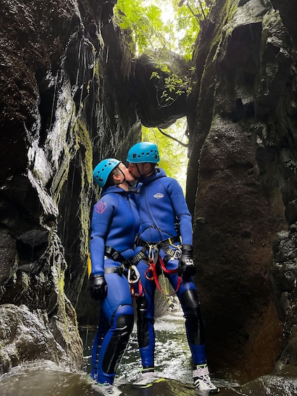 Two people in blue climbing gear standing in a rocky cave with water flowing. 5