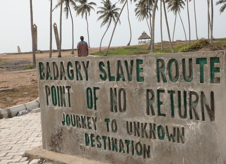 A sign with the text 'BADAGRY SLAVE ROUTE POINT OF NO RETURN JOURNEY TO UNKNOWN DESTINATION'. 1