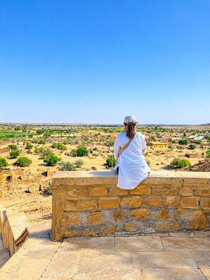 A person sitting on a stone wall overlooking a landscape with wind turbines and scattered buildings. 5