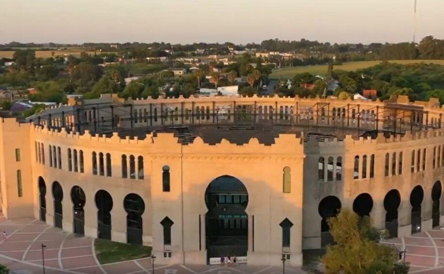A large, historic building with arches and a central entrance, surrounded by a paved area and greenery. 2