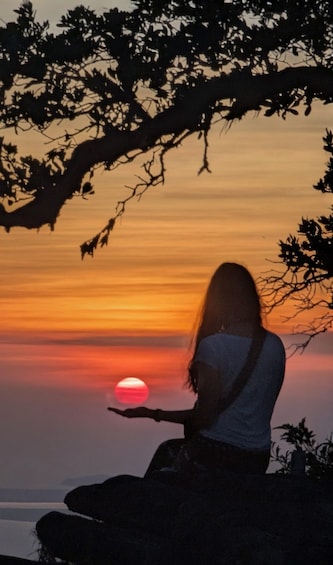 A person sitting on a rock at sunset with a sunset in the background. 5