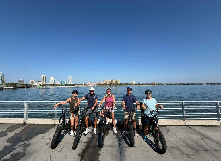 A group of people on bicycles by a waterfront with a city skyline in the background. 5