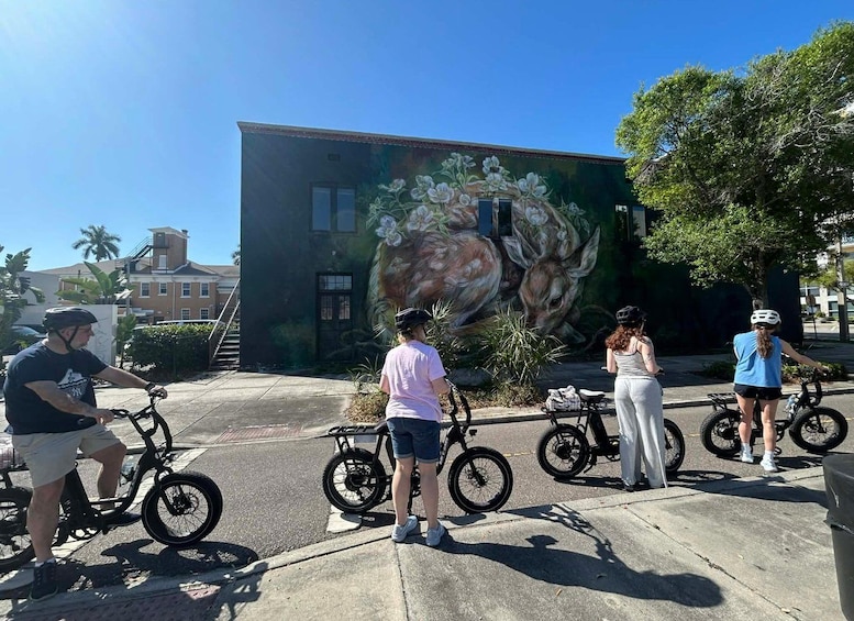 A mural of a deer on a building, a person on a bicycle, and another person on a tricycle. 3